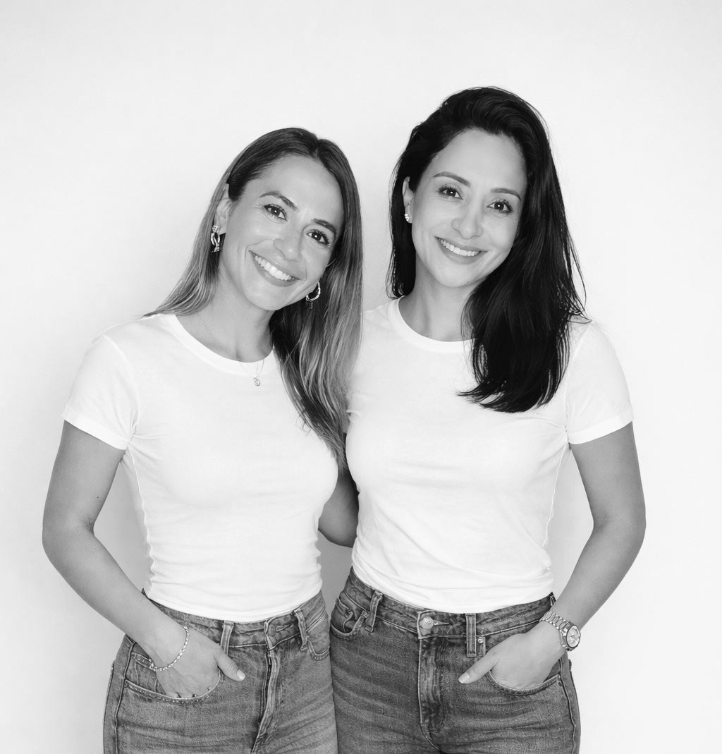 Two women wearing white t-shirts and jeans standing against a plain background